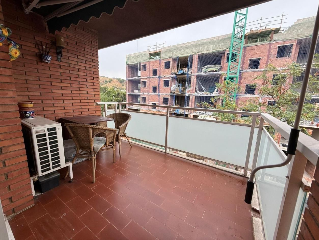 Balcón con mesa, sillas y aire acondicionado. Vista a un edificio en construcción y zonas verdes.