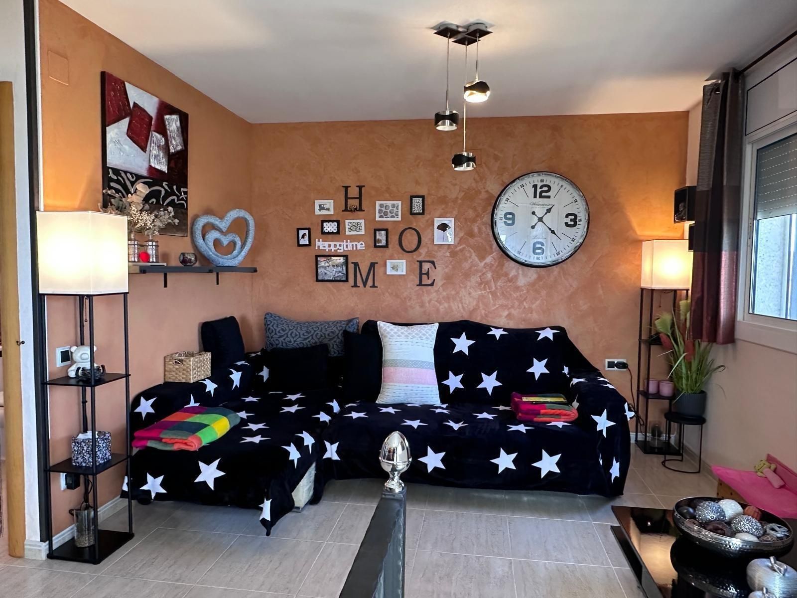 Sala de estar con sofá con estampado de estrellas, paredes naranjas y detalles decorativos, incluido un reloj grande y arte de pared.