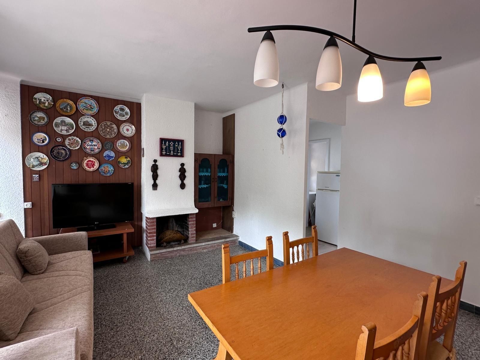 Sala de estar con sofá marrón, TV, mesa de madera y platos decorativos en la pared.