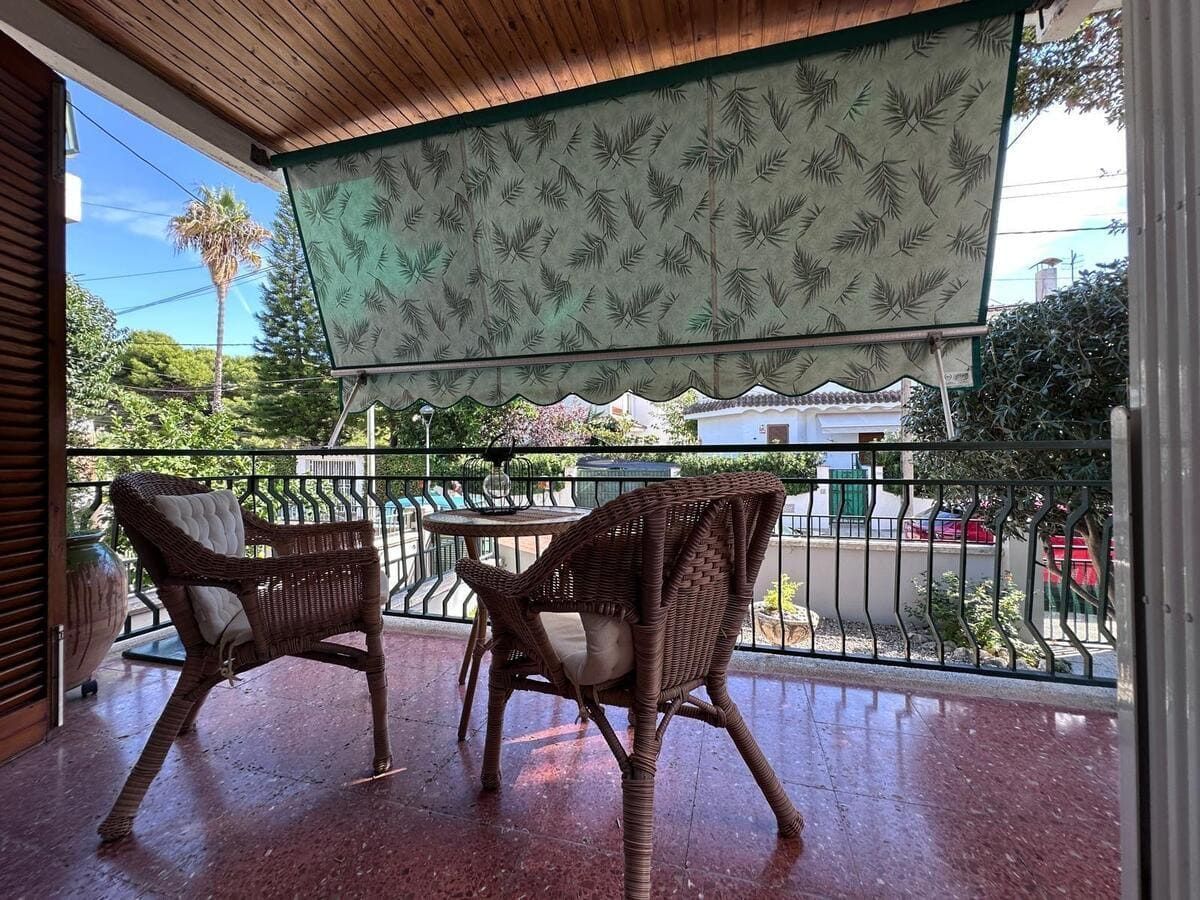 Balcón con dos sillas de mimbre, mesa pequeña y toldo retráctil con vista a un vecindario.