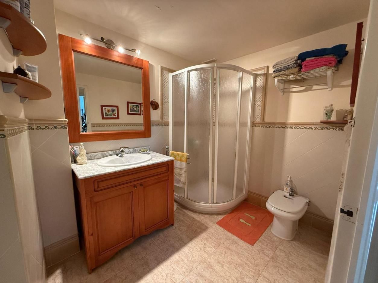 Baño con tocador, ducha e inodoro. Mueble naranja, espejo grande y ducha de cristal esmerilado.