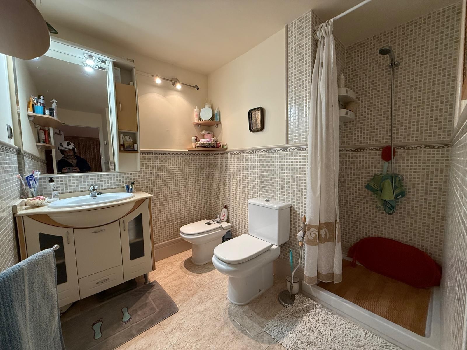 Baño con inodoro, bidé, ducha y lavabo. Paredes de azulejos en tonos beige y blanco.