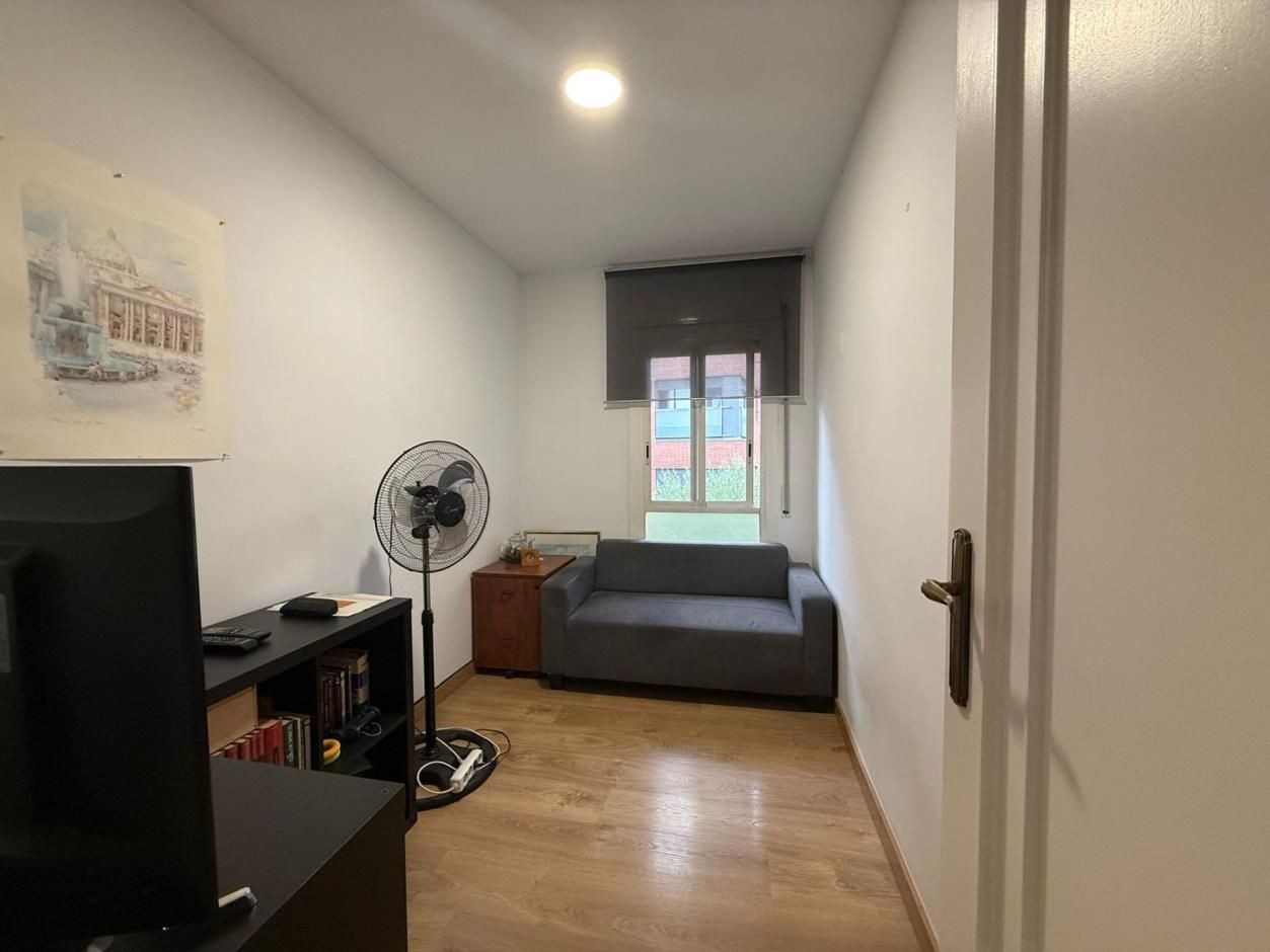 Habitación pequeña con sofá, ventilador, escritorio y obras de arte.