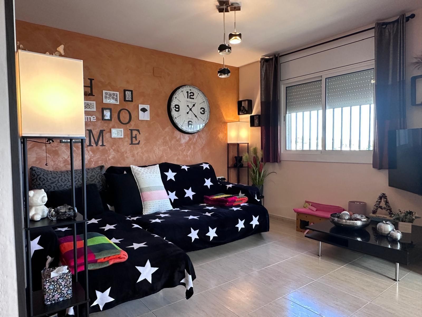 Sala de estar con sofá negro con estampado de estrellas, pared naranja con decoración 