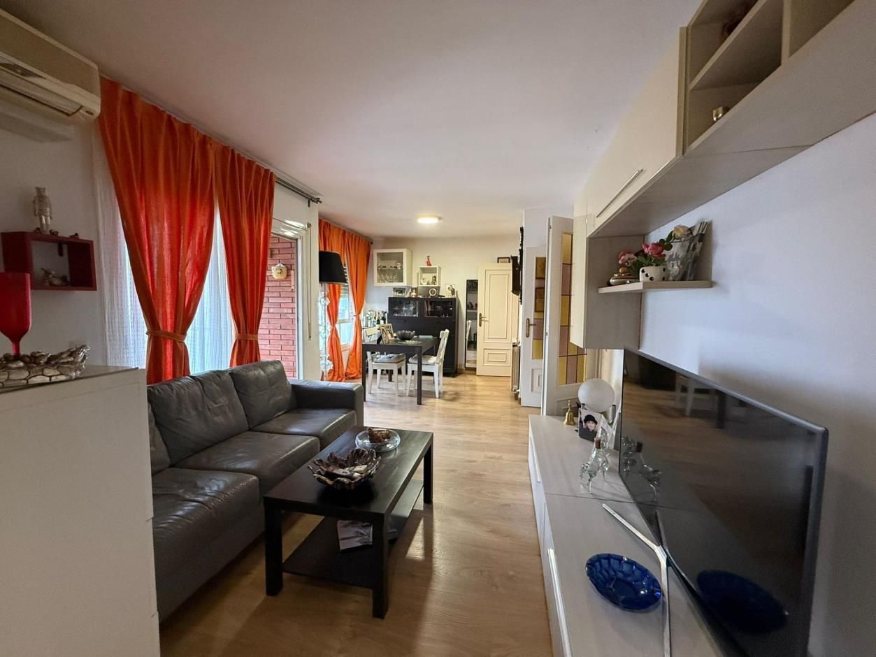 Sala de estar con cortinas naranjas, sofá gris y televisor. Al fondo se ve un comedor.