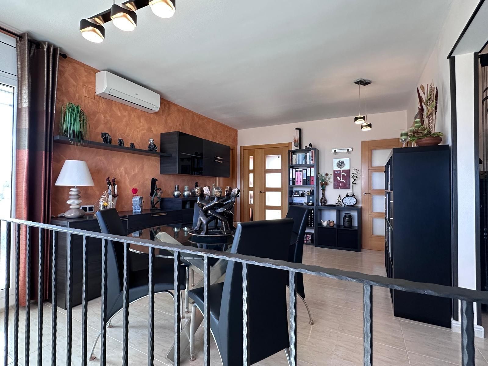 Comedor moderno con muebles negros, pared naranja y estantes decorativos.