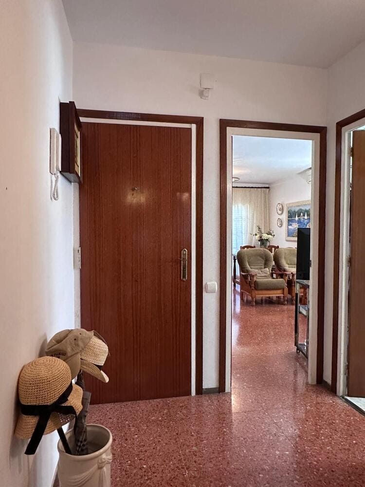 Pasillo con suelo jaspeado rojo, puertas de madera y entrada a salón con muebles.