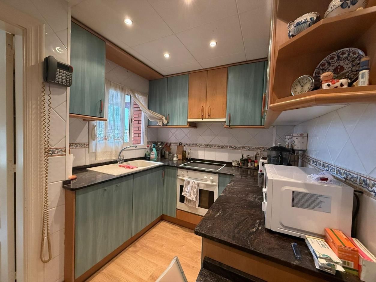 Pequeña cocina con gabinetes color verde azulado, encimeras de granito y microondas.