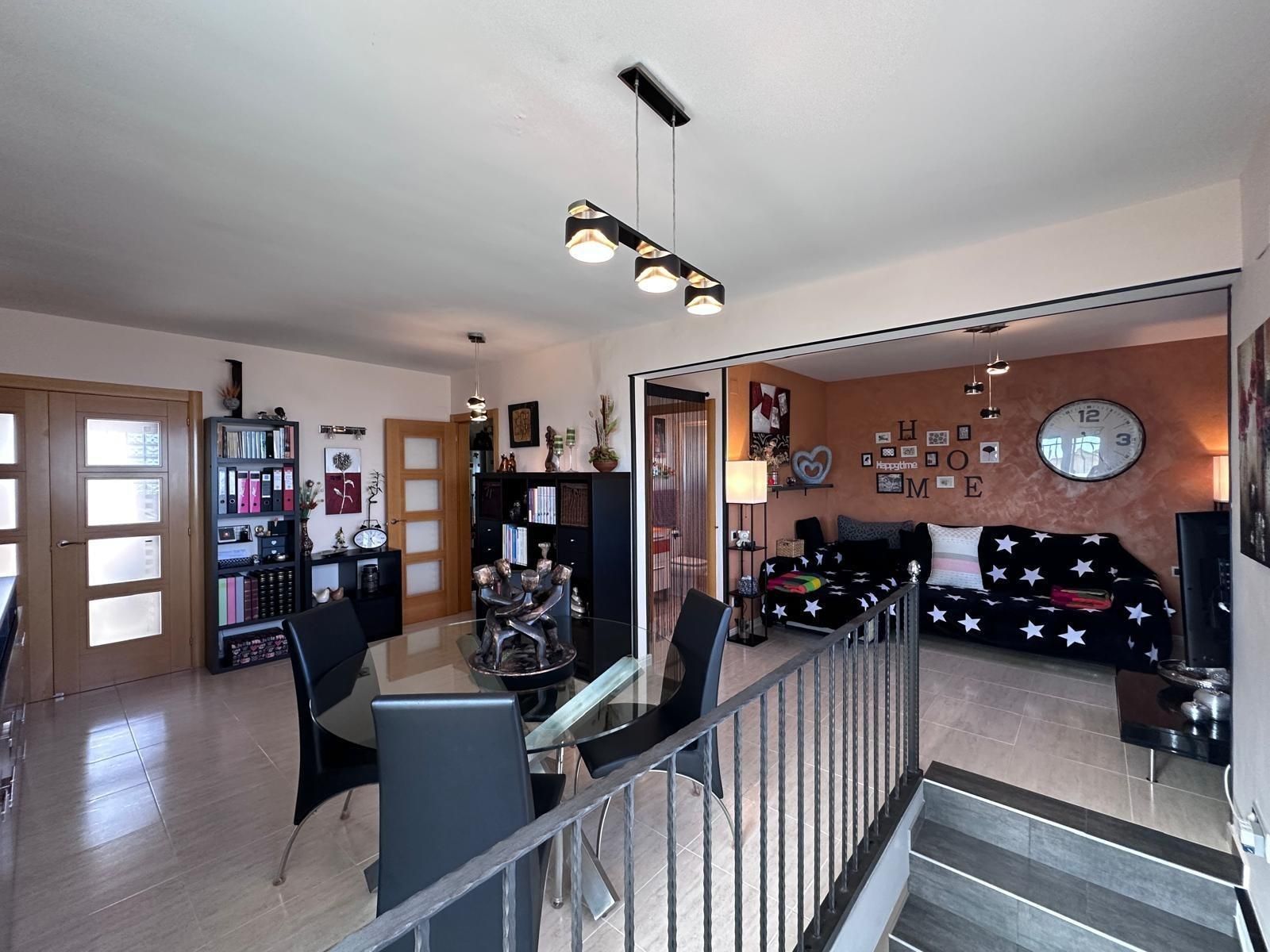 Vista interior de una sala de estar-comedor con escaleras, una mesa y sillas y un sofá.