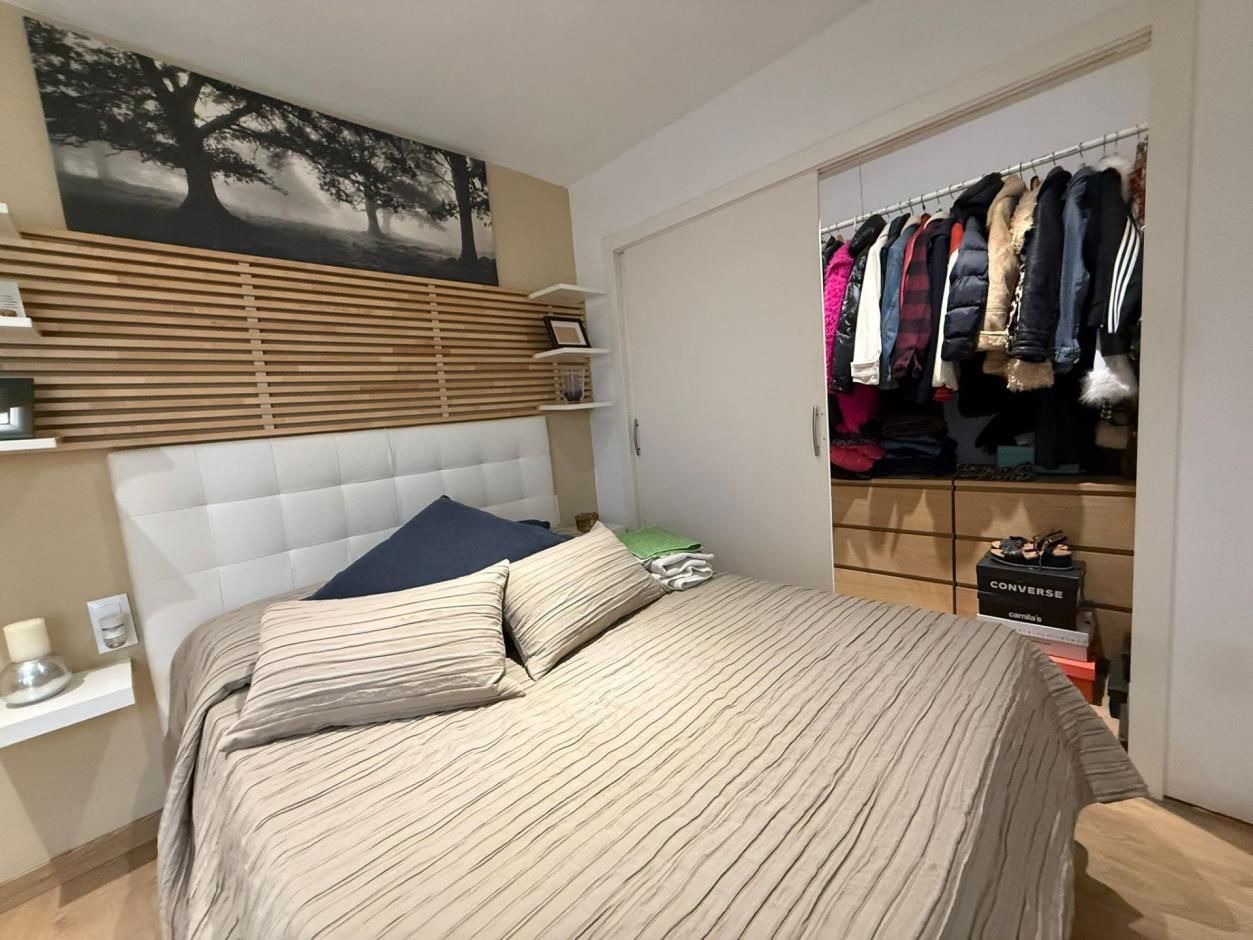 Dormitorio con cama, armario abierto lleno de ropa y arte decorativo en la pared.