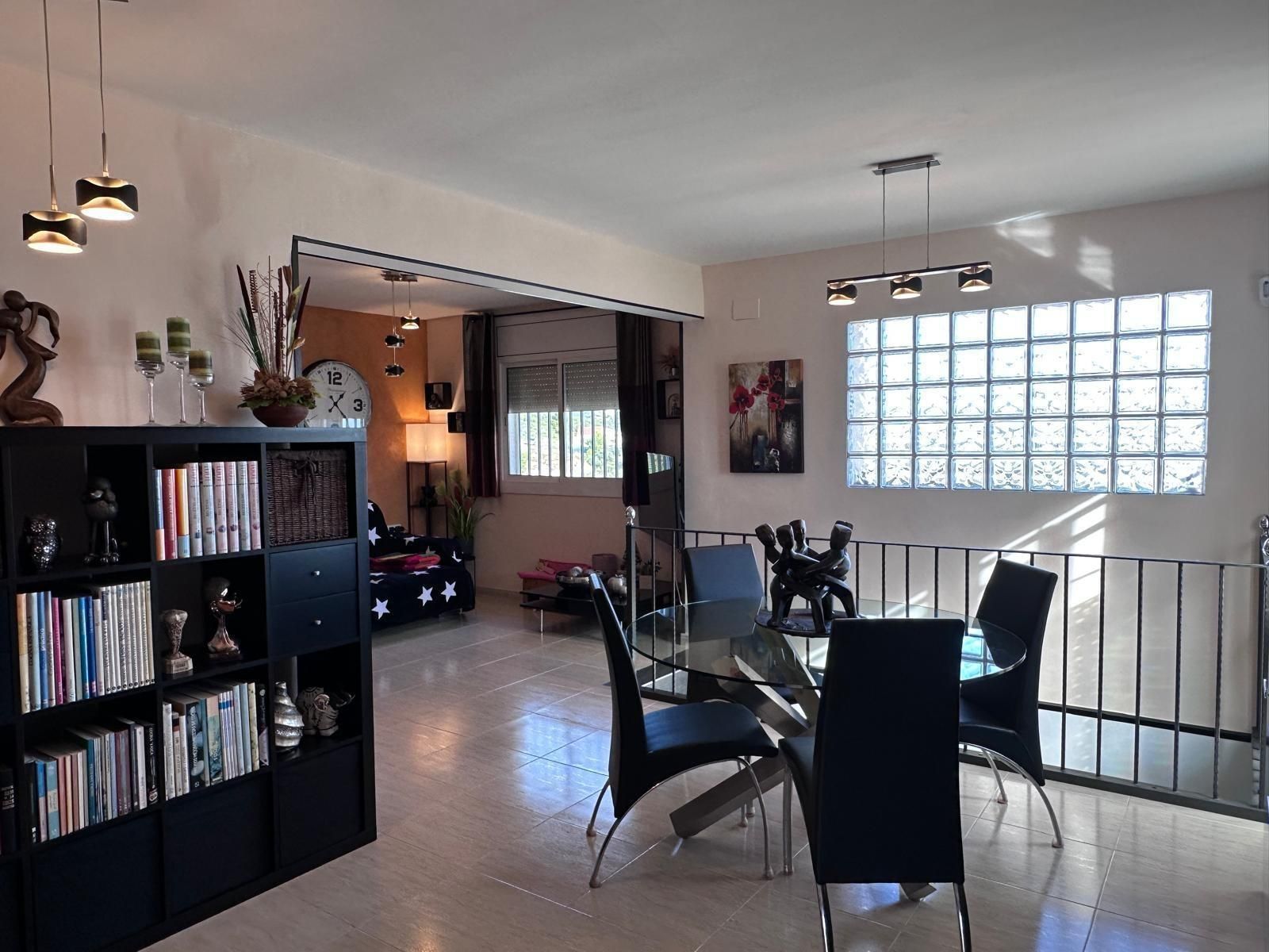 Comedor con mesa negra, sillas, estanterías y ventana de bloques de vidrio.