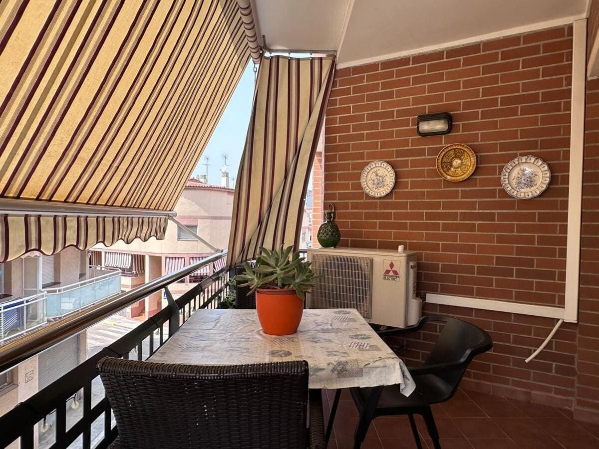 Un balcón con mesa, sillas, pared de ladrillo y toldo. Las plantas y la decoración le dan un toque visual atractivo.