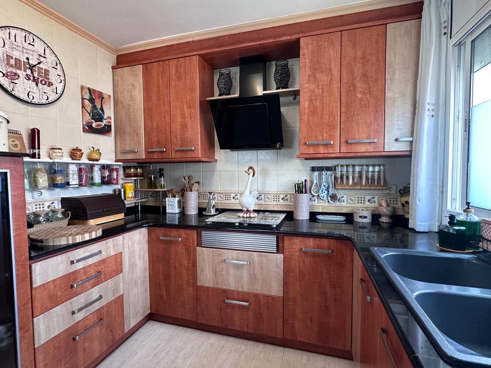 Cocina en forma de U con gabinetes de madera, encimeras negras y un fregadero doble.