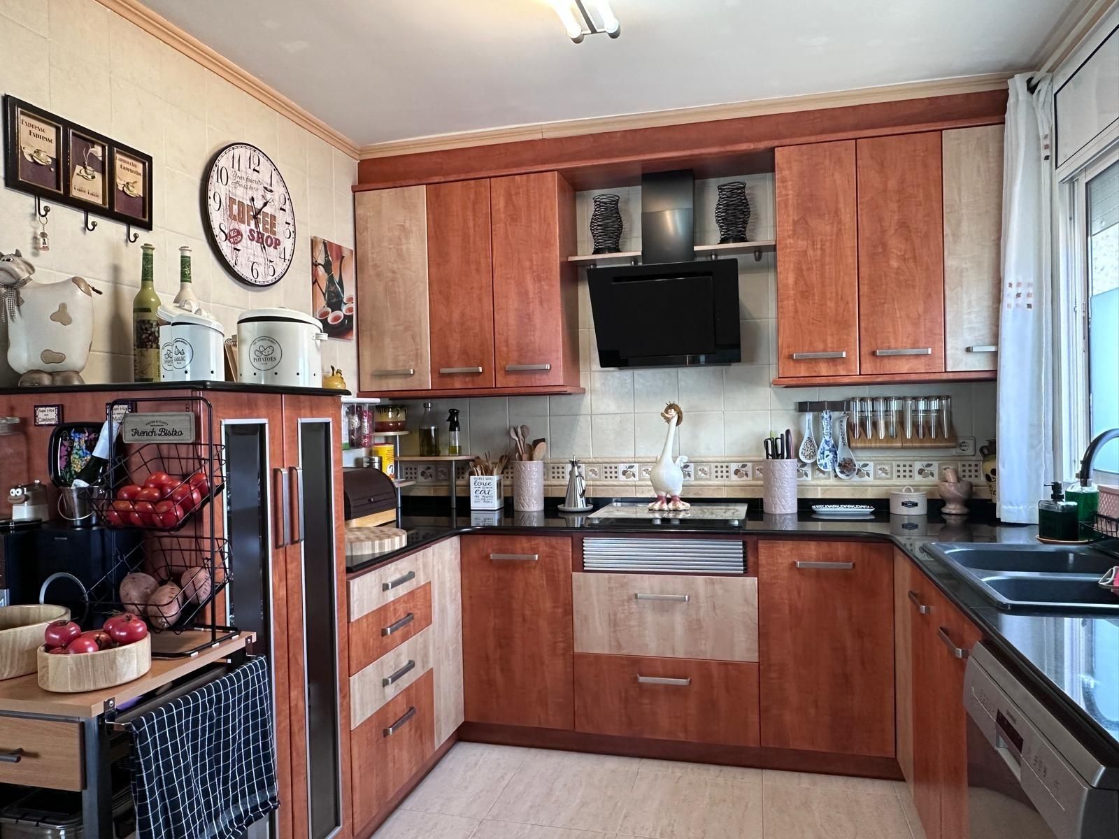 Cocina con gabinetes de madera, encimeras negras y un pequeño televisor montado sobre la estufa.