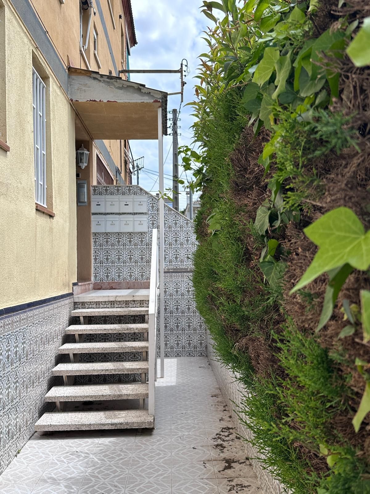 Escaleras metálicas que conducen a la entrada de un edificio, junto a un seto.