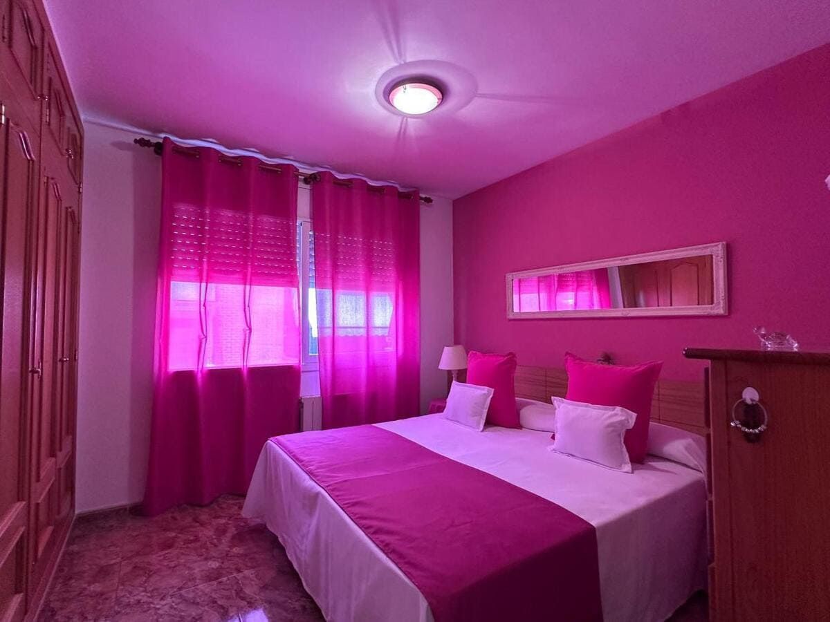 Dormitorio rosa con cama, cortinas y armario.