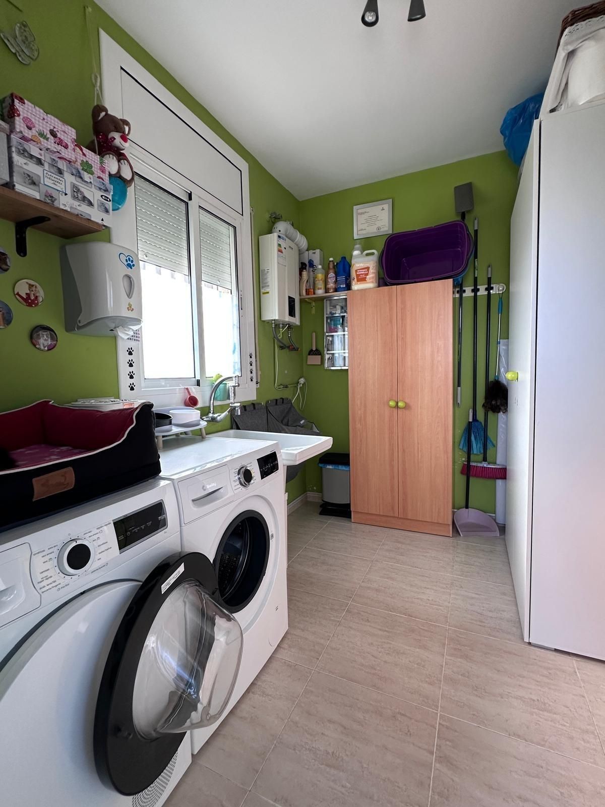 Lavandería con lavadora, secadora, fregadero, armario y artículos de limpieza contra una pared verde.