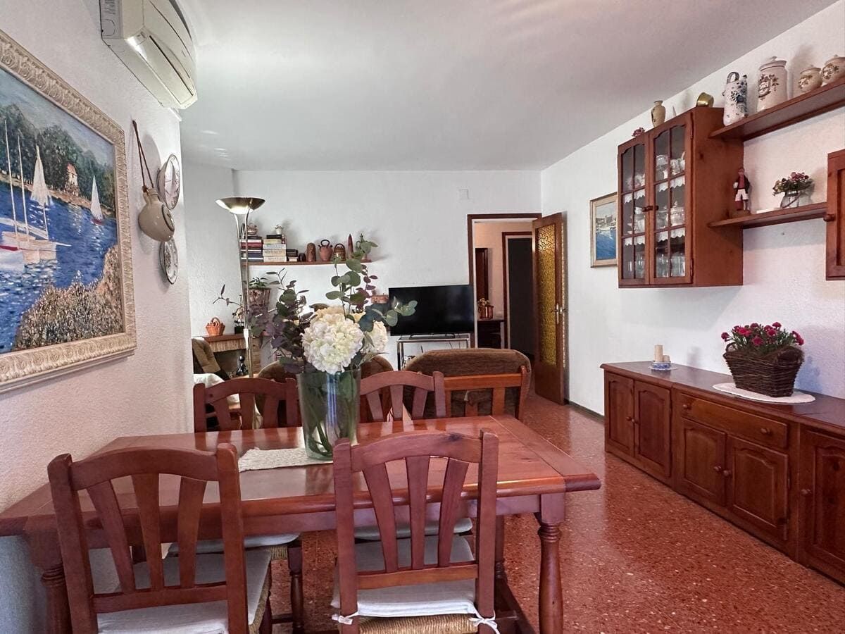 Comedor con mesa, sillas y armario de madera. Suelo de baldosas rojas, paredes blancas y obras de arte.