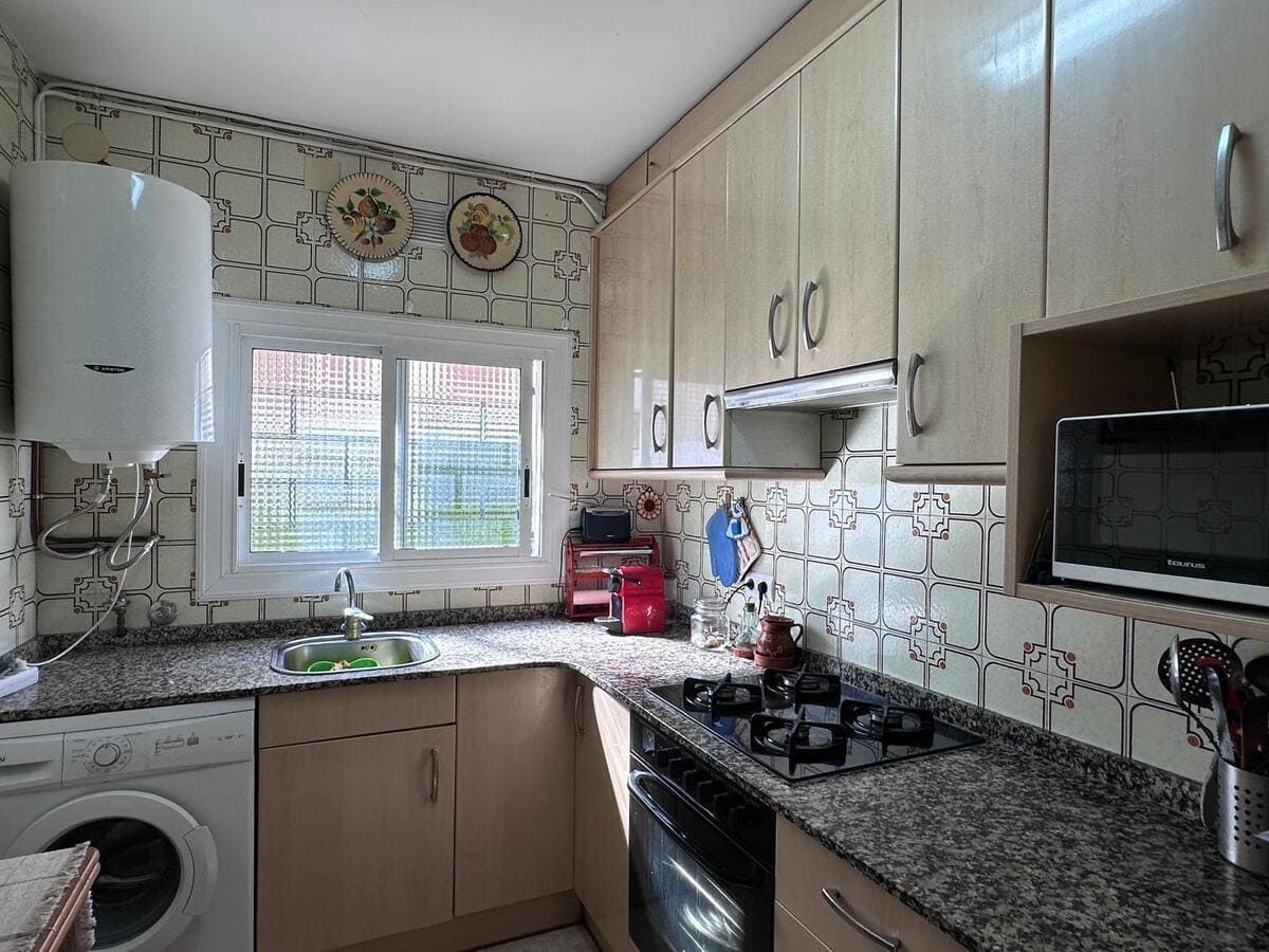 Cocina con gabinetes de color beige, encimeras de granito y protector contra salpicaduras de azulejos; una ventana y electrodomésticos también son visibles.