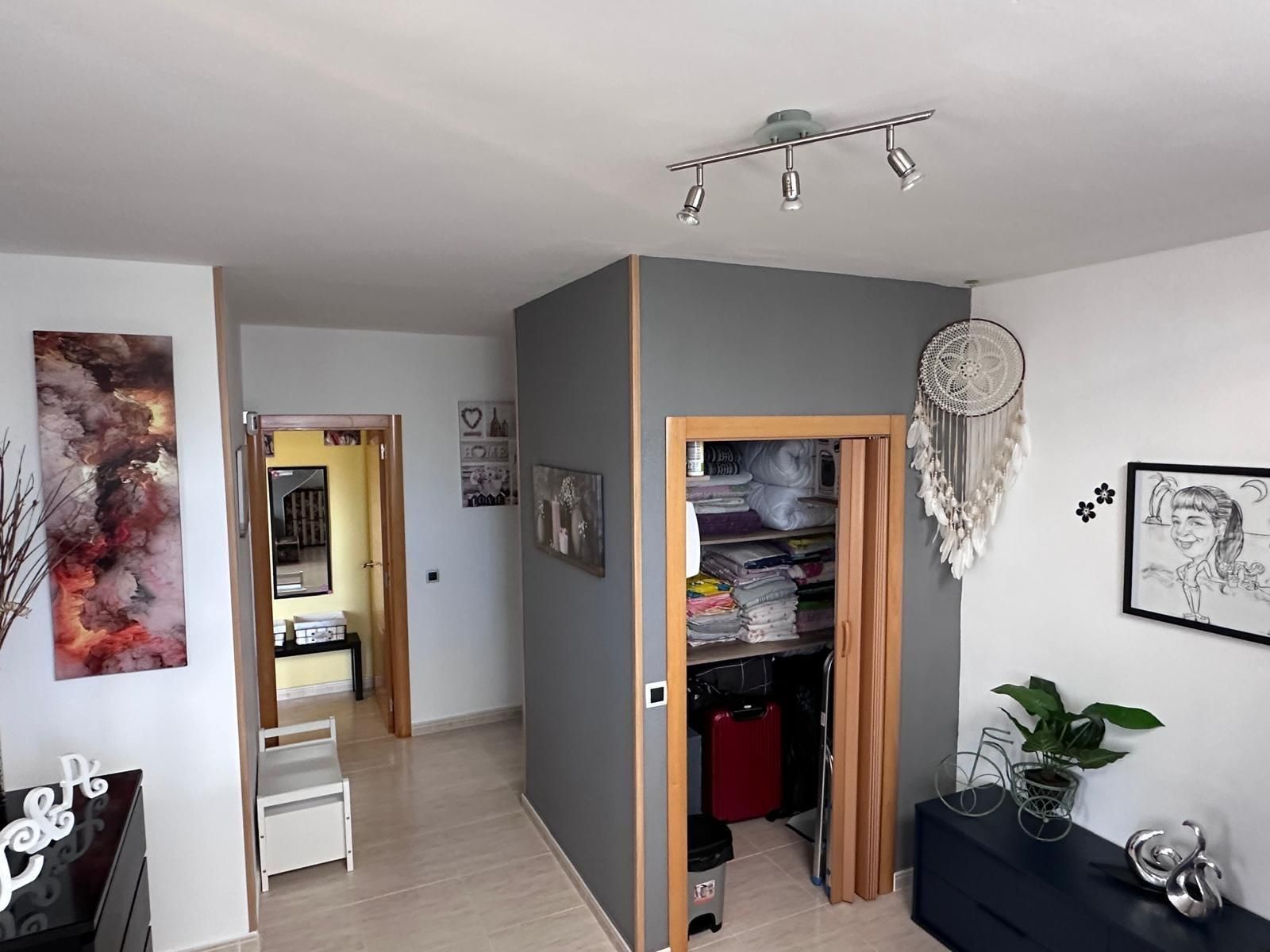 Pasillo con puertas y armario de almacenamiento; paredes grises, obras de arte, banco blanco y atrapasueños.