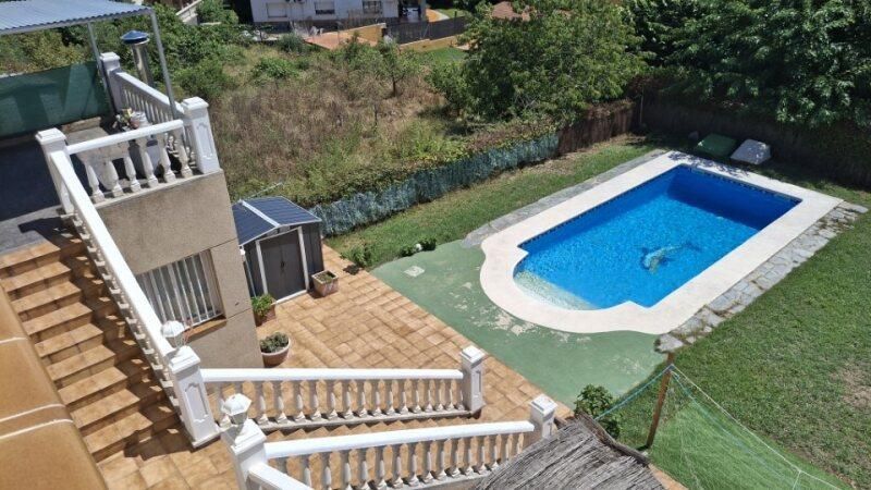 Patio trasero con piscina, patio, césped y casa. Agua azul en la piscina, césped verde, patio de piedra y edificio de color claro.