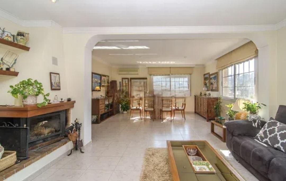 Sala de estar con chimenea, sofá, comedor y ventanas; luz natural.