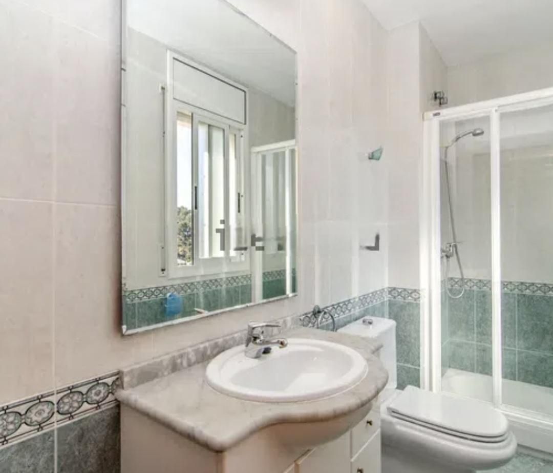 Baño con lavabo, inodoro y ducha. Azulejos y molduras en tonos claros.