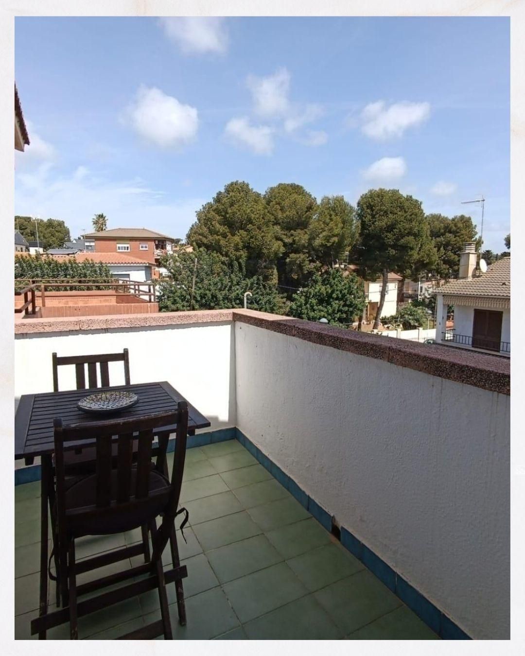 Un balcón con una mesa y sillas y árboles al fondo.