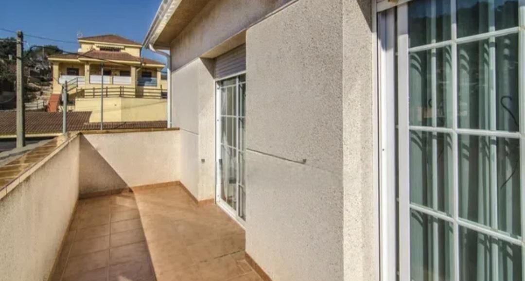 Exterior de una casa con un pequeño balcón, paredes y ventanas blancas; día soleado.