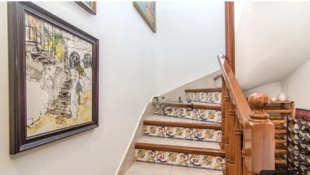 Escalera con contrahuellas de azulejos decorativos y pasamanos de madera. Una obra de arte cuelga de la pared blanca.