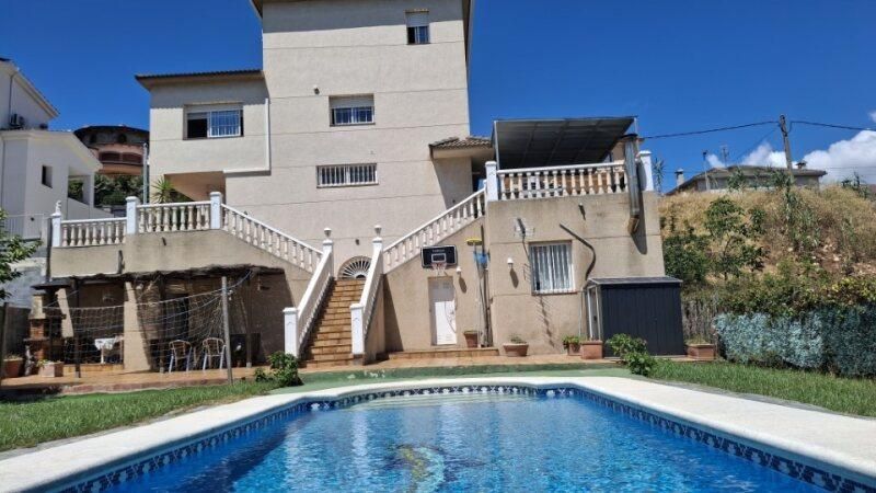 Casa con piscina. Edificio de dos plantas con piscina al frente, día soleado.
