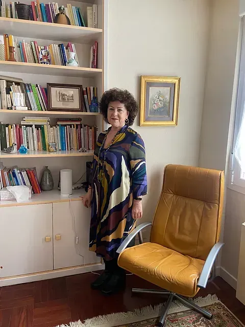 Una mujer está parada junto a una silla amarilla en una habitación con estanterías.