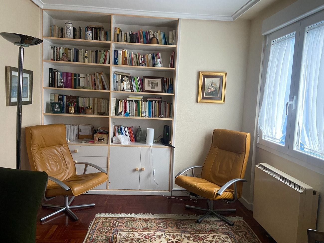 Una sala de estar con dos sillas y una estantería llena de libros.