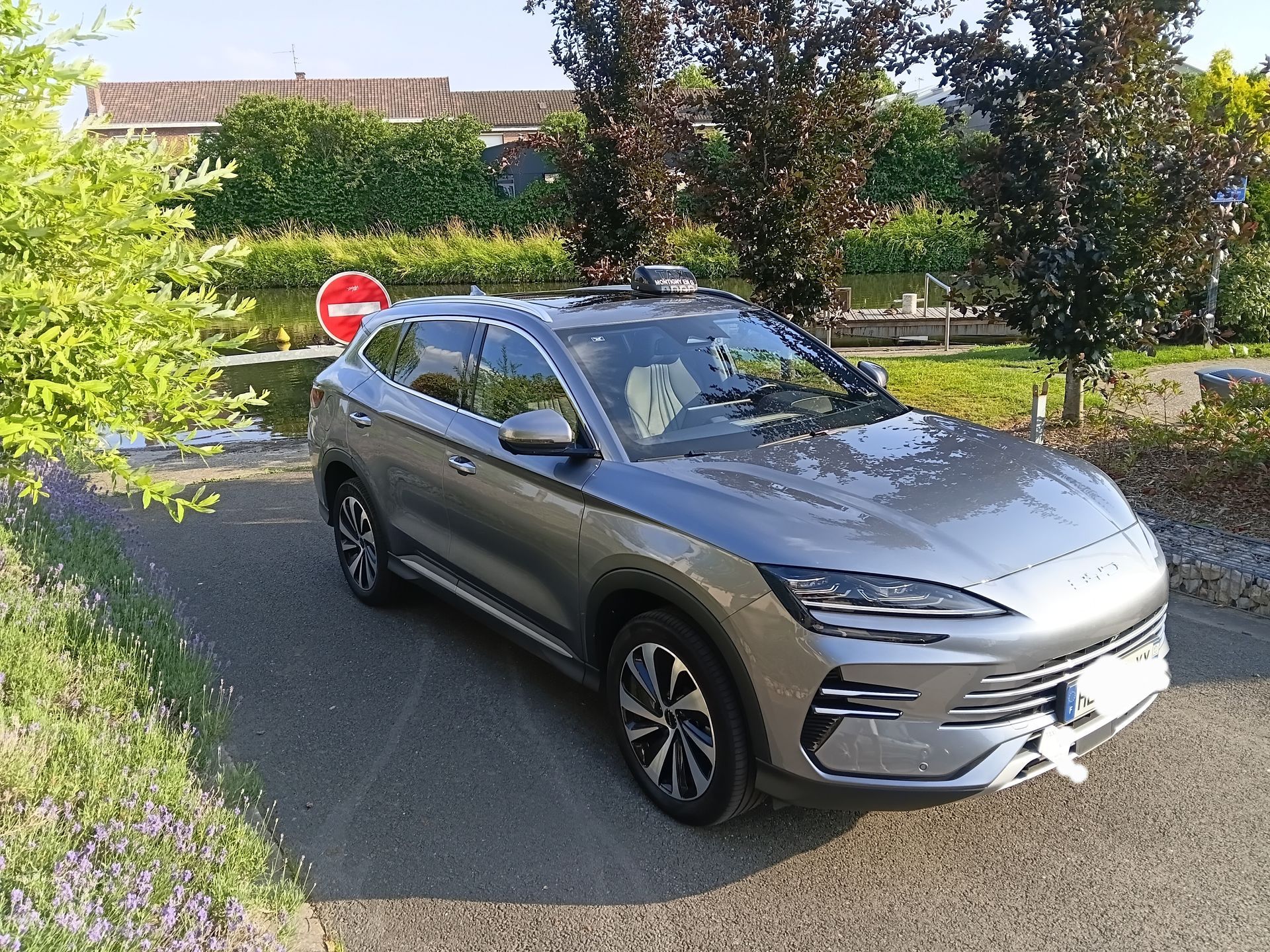 SUV gris stationné dans une rue résidentielle, à côté d'arbres et d'un panneau stop.