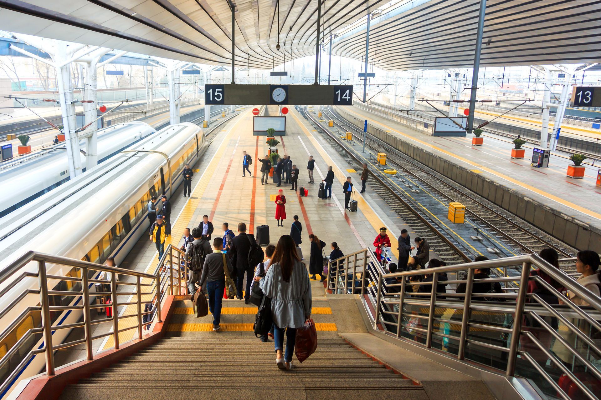 Quai de gare bondé, les voyageurs descendant les escaliers sous un grand auvent.