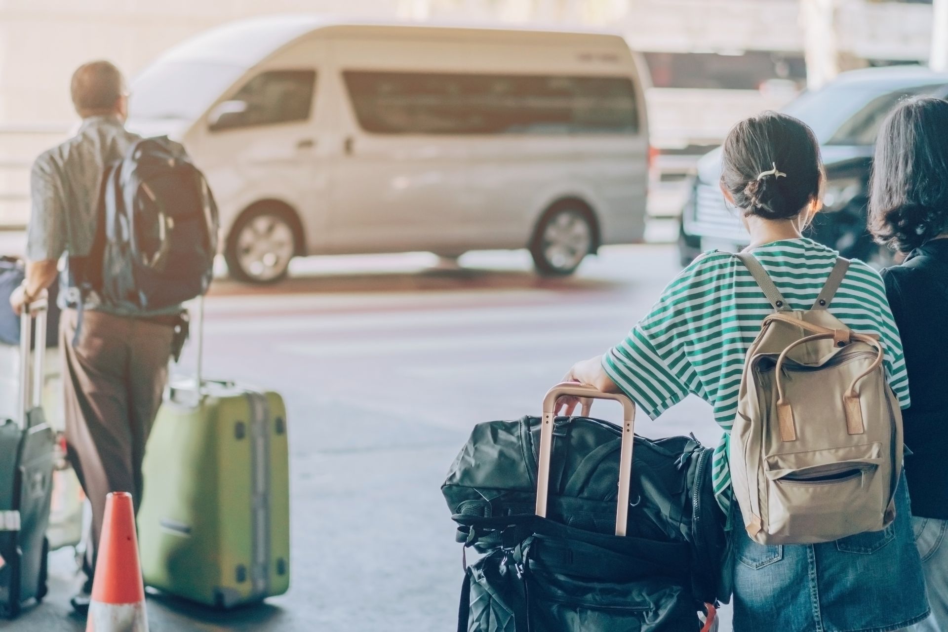 Des voyageurs avec leurs bagages attendent près d'une navette sur le trottoir d'un aéroport.