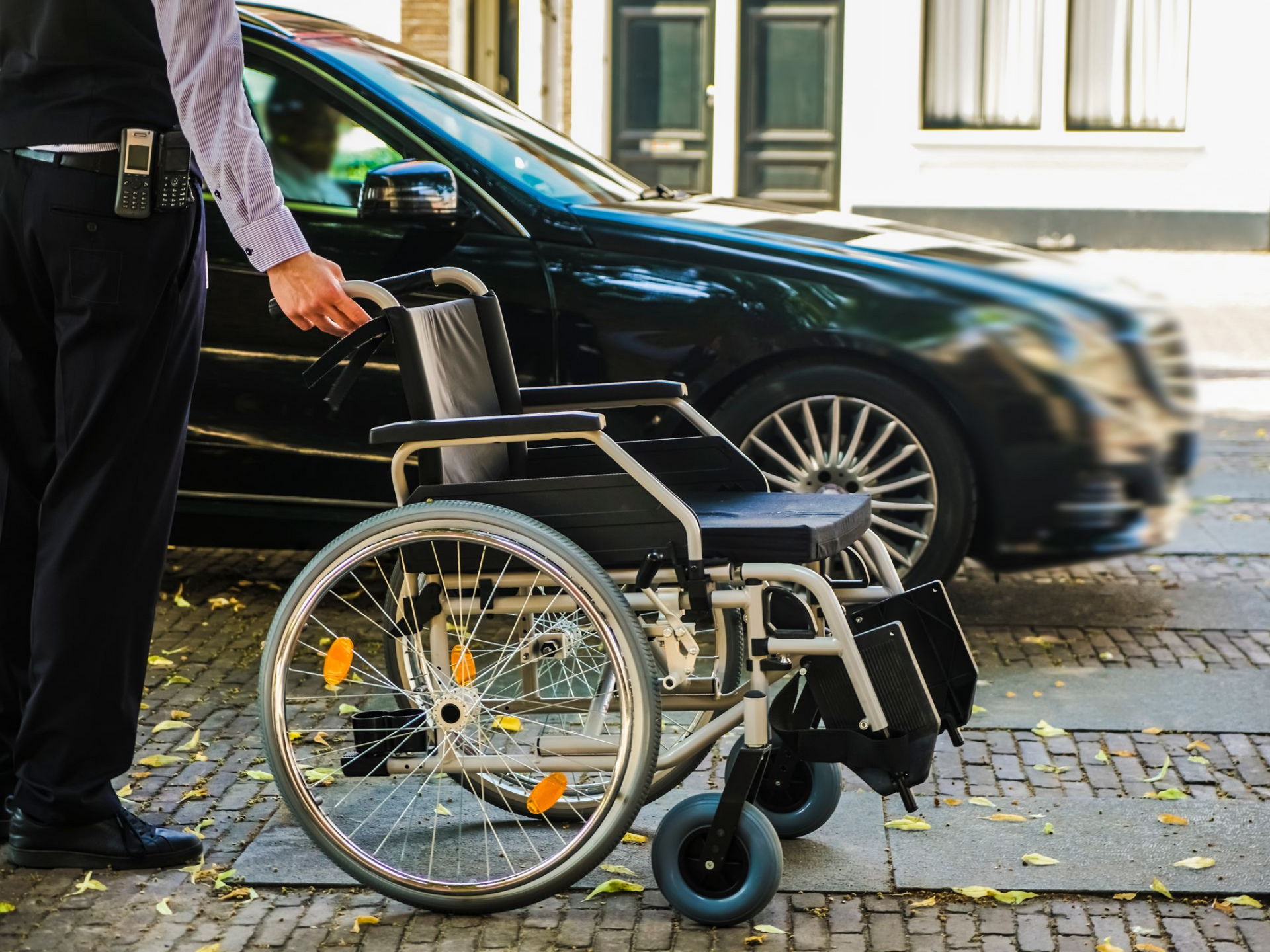 Une personne se tient debout à côté d'un fauteuil roulant dans une rue de la ville, avec une voiture noire garée en arrière-plan.