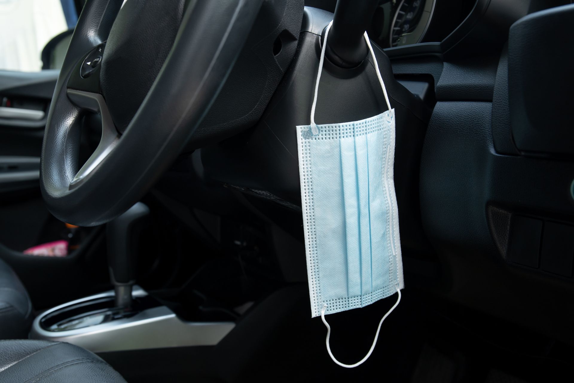 Un masque bleu accroché au volant d'une voiture dans un intérieur sombre.