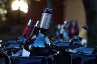 Botellas de vino en cubiteras negras sobre una mesa, con un fondo bokeh desenfocado.