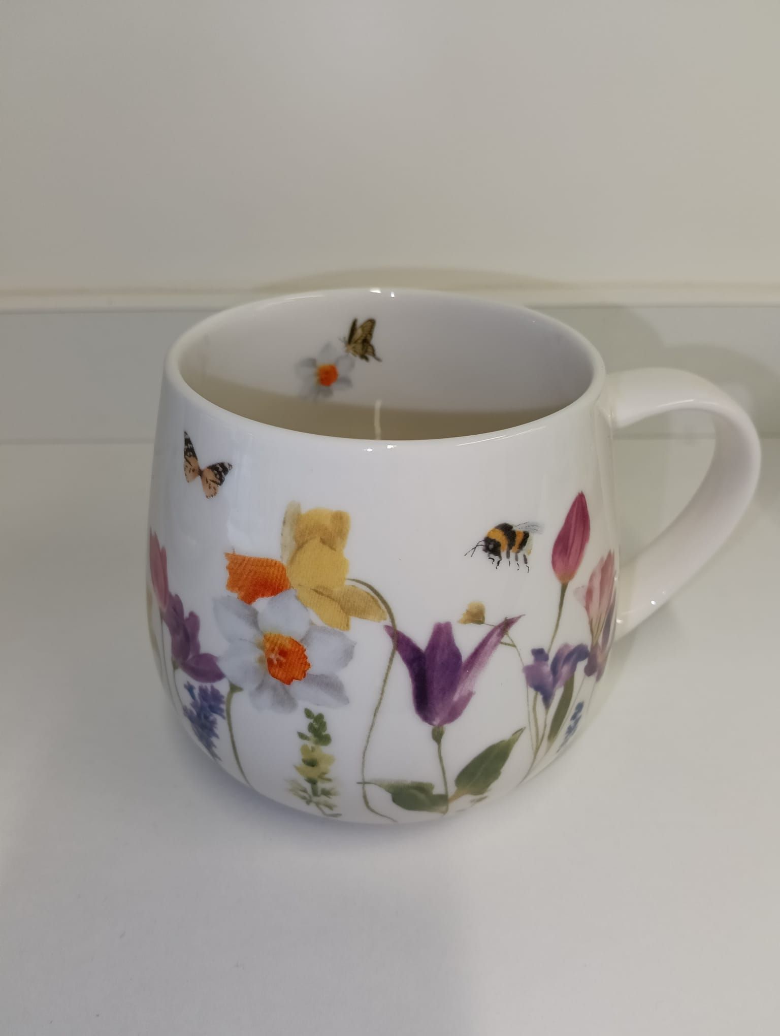 Taza blanca con coloridos diseños florales y de mariposas sobre una superficie clara.