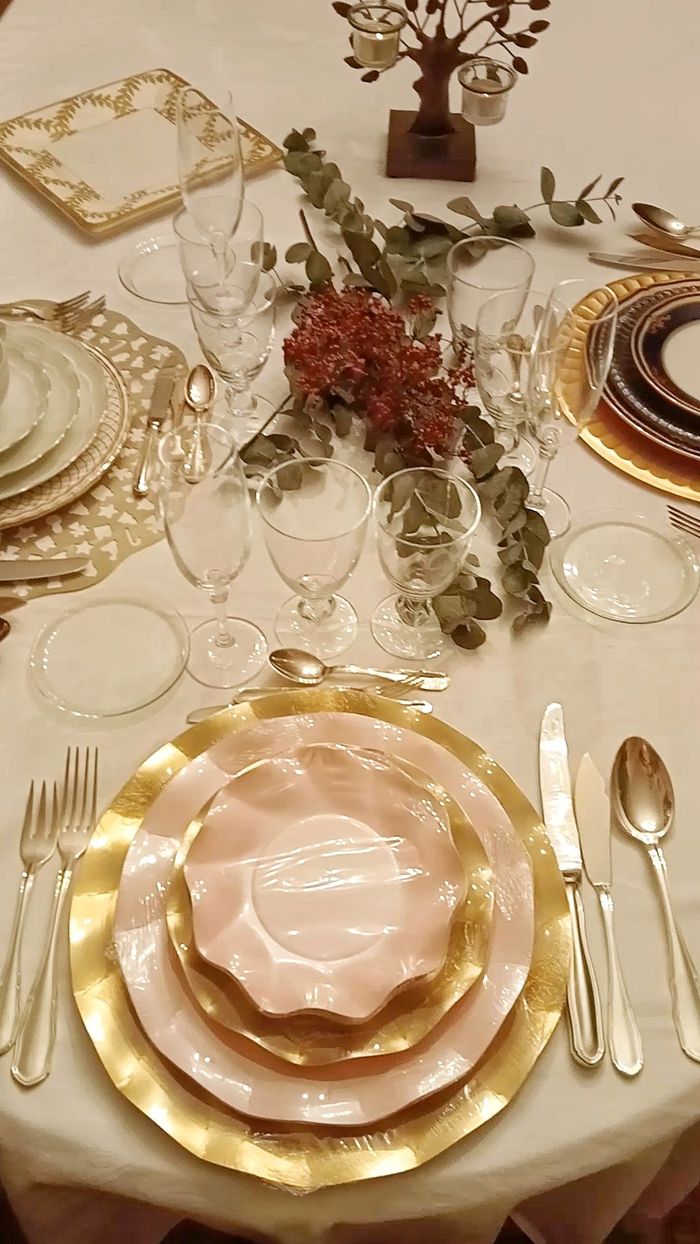 Elegante mesa de comedor con platos con borde dorado, servilletas rosas, cristalería y un centro de mesa floral.