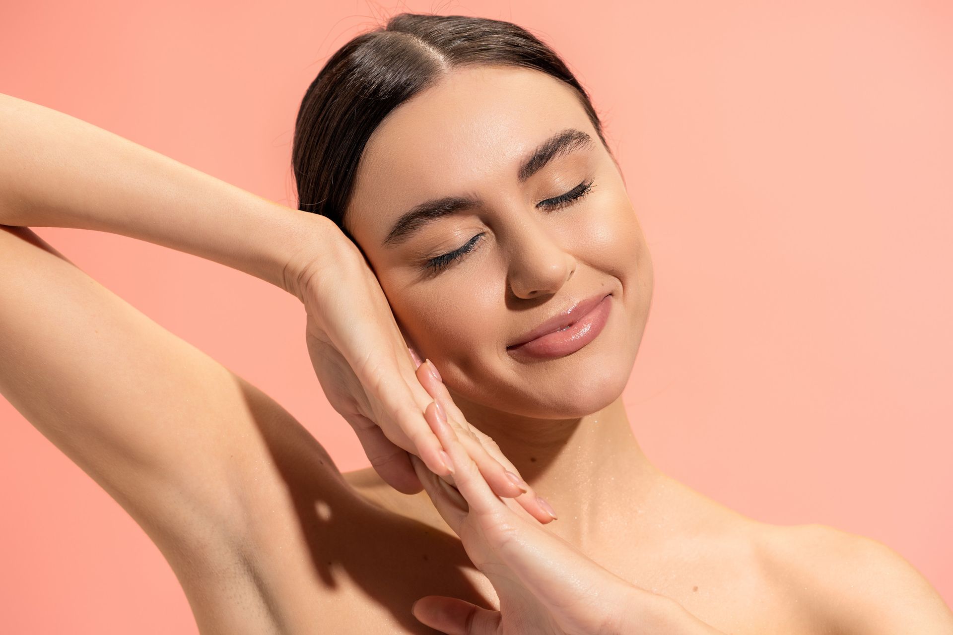 Mujer con los ojos cerrados sonriendo, con las manos enmarcando su rostro, sobre un fondo de color melocotón.