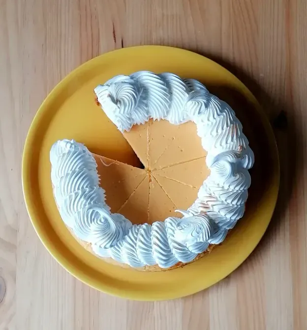 Pastel con glaseado de merengue blanco sobre un plato amarillo, falta una rebanada.
