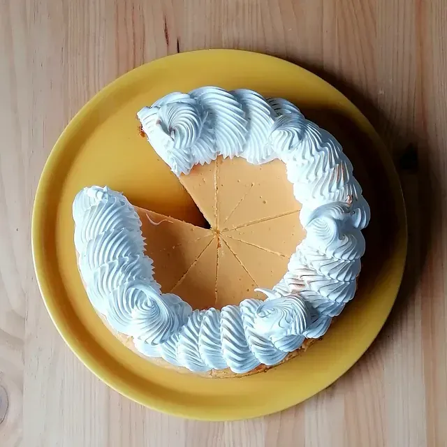 Un pastel redondo, de color naranja, del que se ha quitado una rebanada y decorado con remolinos de glaseado blanco, sobre un plato amarillo.