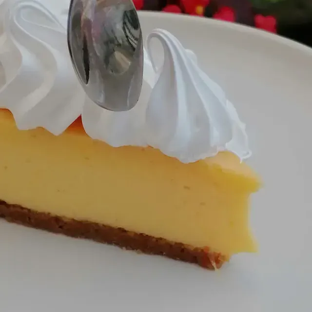 Rebanada de tarta de queso con crema batida blanca, servida con cuchara, en un plato blanco.
