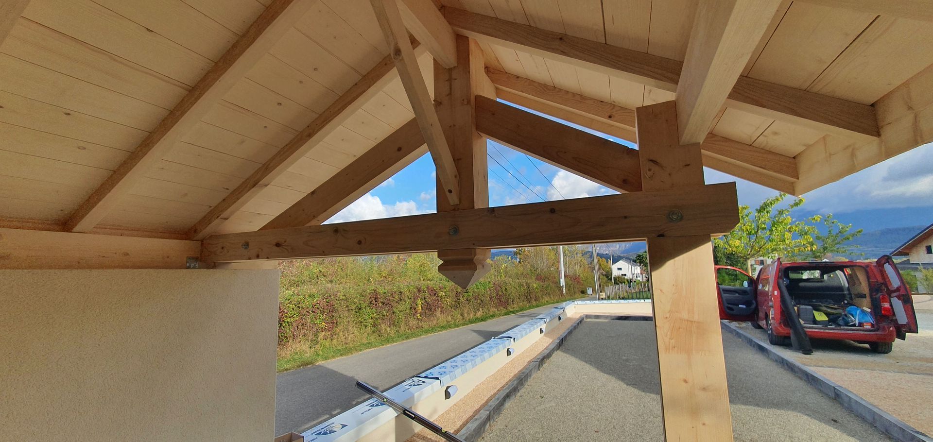 Structure de toit en bois avec vue sur le ciel, la route et une camionnette rouge.