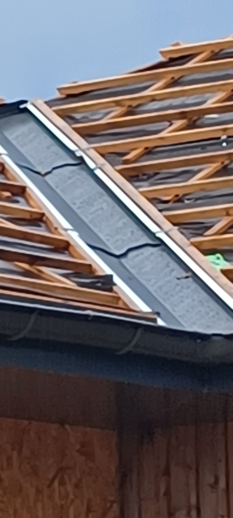 Toit avec poutres en bois, matériau de toiture foncé et gouttière.