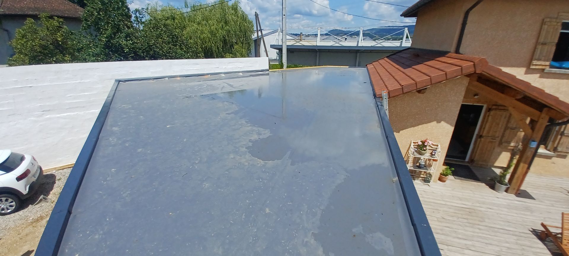 Vue depuis un toit plat surplombant un bâtiment de couleur claire avec un toit marron et une voiture blanche.