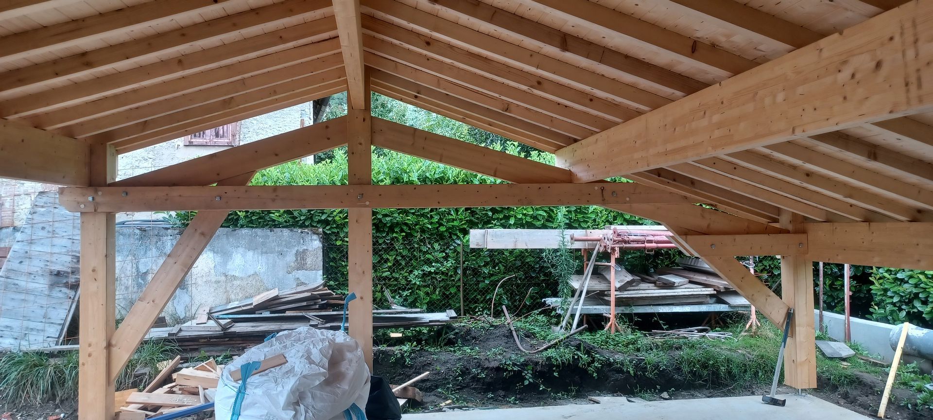 Structure en bois d'un toit en construction, avec poutres et chevrons visibles, à l'extérieur.