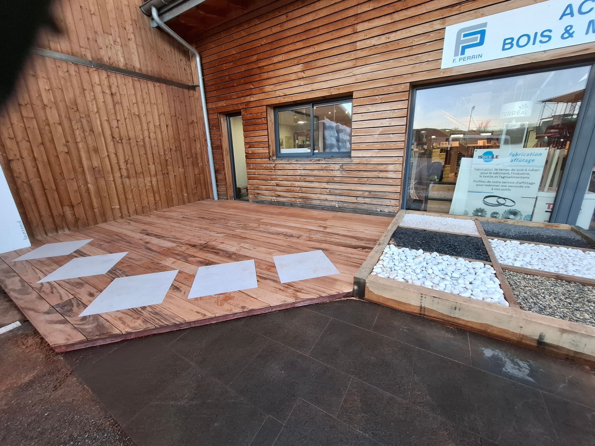 Terrasse en bois avec des dalles carrées de couleur claire et un étalage de pierres d'aménagement paysager à l'extérieur d'un magasin.